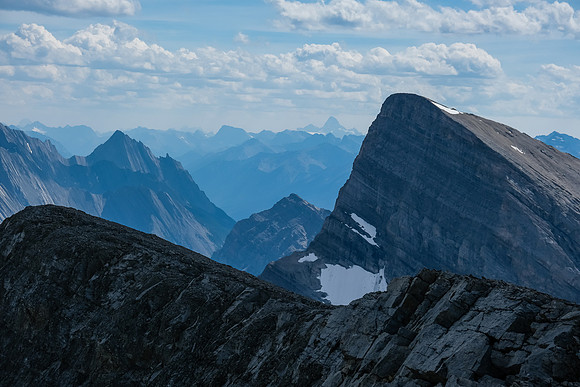 A distant Mount Assiniboine past an unnamed peak over the approach col.