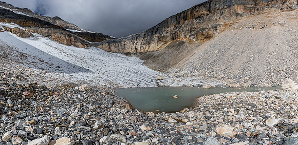 A frozen glacial tarn with the glacier above, littered with rock debris.