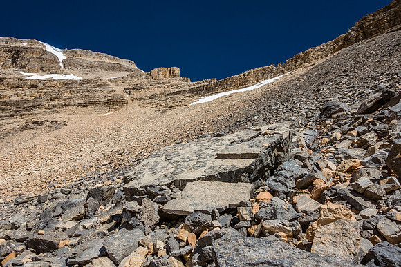 The break in the cliffs is at center rising to the left, the Thompson / Portal col is on the right side of the upper snow patch along the base of the cliffs.