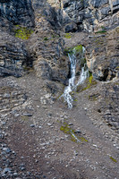 A waterfall bursts out of the cliff above. These rocks are anything but solid...