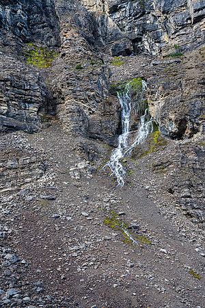 A waterfall bursts out of the cliff above. These rocks are anything but solid...