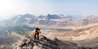 Phil scrambles up the last few feet to the summit of Mount McConnell! All three of the McConnell lakes in the background.