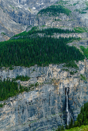 A massive waterfall spouts directly out of a blank cliff face.