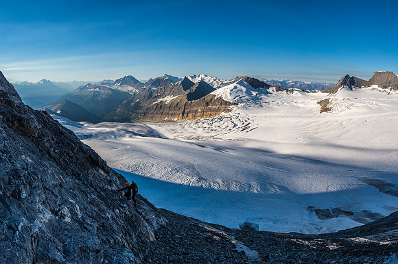 Ferenc climbs up some slabs with the Chess Group across the glacier in the background.