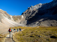 The group passes by a perfectly calm tarn in Larch Valley with Sentinel Pass looming above and Mount Temple looming above.