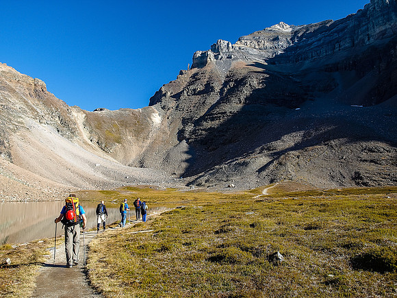 The group passes by a perfectly calm tarn in Larch Valley with Sentinel Pass looming above and Mount Temple looming above.